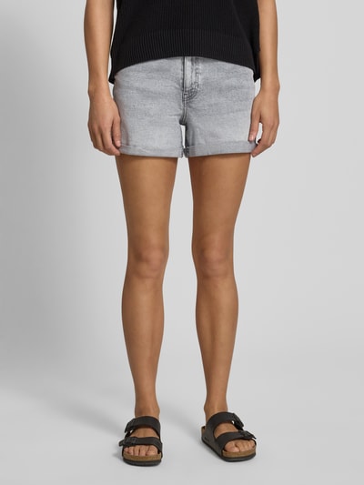 Kobiece model prezentuje szorty jeansowe High Waist Jeansshorts mit Umschlag Modell 'MONI' von Noisy May, mieszanka bawełny i elastanu, wpuszczane kieszenie, brzeg, szerokość w rozmiarze S: 35 cm, długość wewnętrzna nogawki w rozmiarze S: 9 cm, widok całej sylwetki z przodu.