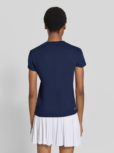 Vrouwenmodel draagt donkerblauw Slim Fit Sport-T-Shirt aus Baumwoll-Mix von Lacoste, dames sport-t-shirt, witte plissérok, Ganzkörperansicht Rückansicht