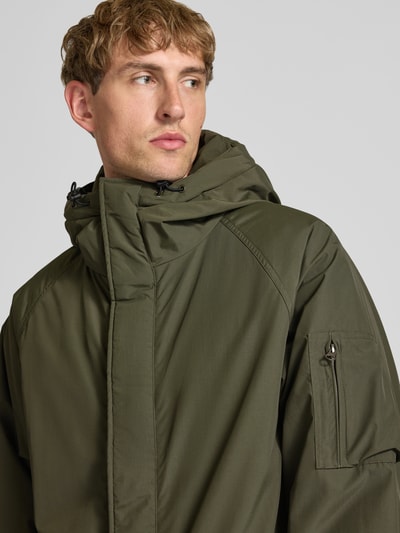 Männermodel trägt olivgrünen Parka mit Pattentaschen Modell 'Stanwood' von Carhartt Work In Progress, Reißverschluss, Nahaufnahme Oberkörper.