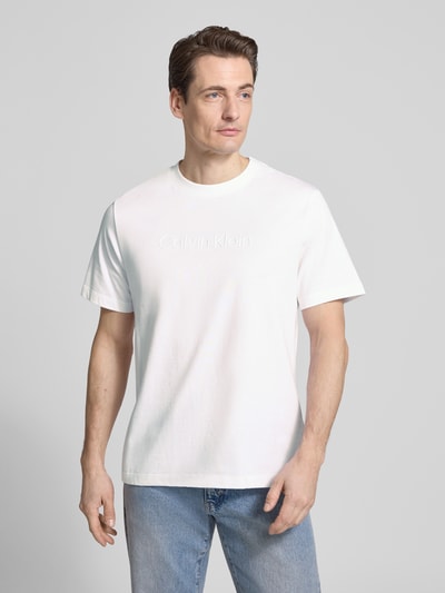 Männermodel trägt T-Shirt mit Rundhalsausschnitt von CK Calvin Klein in Weiß, Herren T-Shirt aus reiner Baumwolle, Regular-Fit, Logo, Ganzkörperansicht von vorne. Rückenlänge bei Größe M: 67 cm.