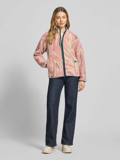 Kobiece modelka nosi kurtkę z polaru 'Fleecejacke im Allover-Look mit Stehkragen' od PEAK PERFORMANCE w wzór na całej powierzchni, krój regular fit, stójka, zamek błyskawiczny, długość tyłu w rozmiarze S: 65 cm, szerokość ramion w rozmiarze S: 52 cm, szerokość klatki piersiowej w rozmiarze S: 53 cm, długość rękawów w rozmiarze S: 56 cm, kolor różowy i niebieski, faktura miękka, widok całej sylwetki z przodu.