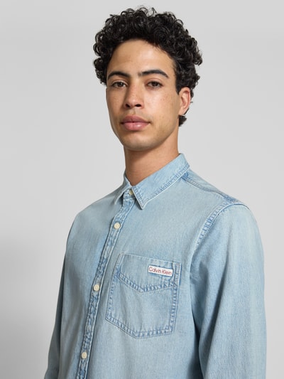 Männermodel trägt Regular Fit Jeanshemd aus reine Baumwolle von Calvin Klein Jeans in denimlook met labelpatch, borstzak, kentkraag, doorlopende knoopsluiting, lange mouwen met manchet met één knoop, materiaal puur katoen, Nahaufnahme Oberkörper.