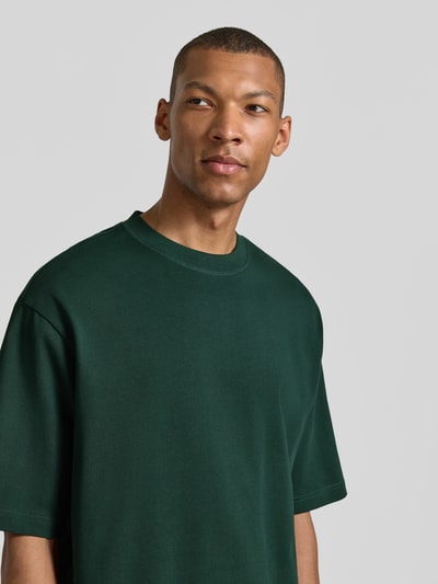 Męski model nosi Regular Fit T-Shirt aus reiner Baumwolle Modell 'HASPEN' von SELECTED HOMME, ciemnozielony, gładka faktura, zbliżenie na górną część ciała.