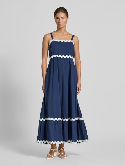 Frauenmodel trägt Midikleid mit Karree-Ausschnitt und Wellensaum von Apricot, Reine Baumwolle, Taillierter Schnitt, Breite, verstellbare Träger, Haken-Reißverschluss, Smok-Detail, Dunkelblau mit weißen Akzenten, fließende Textur, Ganzkörperansicht von vorne.