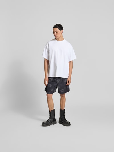 Männermodel trägt Shorts aus reiner Viskose von Officine Générale in Schwarz mit Print, elastischem Bund und Tunnelzug, Ganzkörperansicht von vorne.