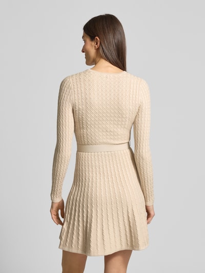 Vrouwenmodel draagt Mini-jurk uit viscosemix in tricotlook model 'Hana' van Guess, getailleerde pasvorm, tailleband, met lange mouwen, ronde hals, ruglengte maat S 89 cm, borstwijdte maat S 28 cm, mouwlengte maat S 60 cm, lichtbeige met textuur, geheel van achteren.