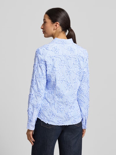 Modelka nosi HBK Zümdholzstreifen Streifen Bluse mit Blumen Applikationen od Christian Berg Woman, niebiesko-białe paski, aplikacje kwiatowe, luźny krój, koszulowy kołnierzyk, z mieszanki materiałów z bawełną, długość tyłu 62 cm, długość rękawa 60 cm, widok całej sylwetki od tyłu.