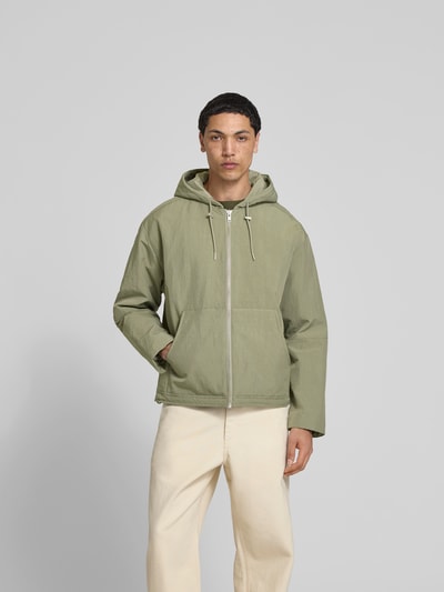 Männermodel trägt Regular Fit Jacke mit Kapuze von WON HUNDRED in hellem Grün, geteilter Känguru-Tasche, Reißverschluss, Tunnelzug, Ganzkörperansicht von vorne.
