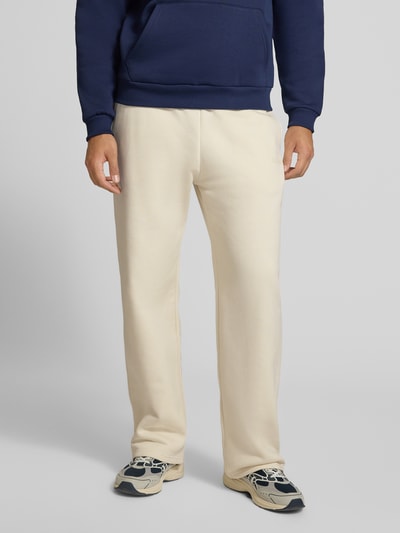 Männermodel trägt Straight Fit Sweatpants aus Baumwoll-Mix mit Label-Detail von REVIEW, cremefarben, elastischer Bund, Eingrifftaschen, Ganzkörperansicht von vorne. Herren Sweatpants, Innenbeinlänge bei Größe M 80 cm.
