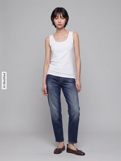 Frauenmodel trägt weißes Tanktop aus Baumwoll-Elasthan-Mix von OPUS, taillierter Schnitt, Rundhalsausschnitt, zur Jeans kombiniert, Ganzkörperansicht von vorne, Modell Daily E, Rückenlänge bei Größe 36 54 cm, KI-modifiziertes Bild.