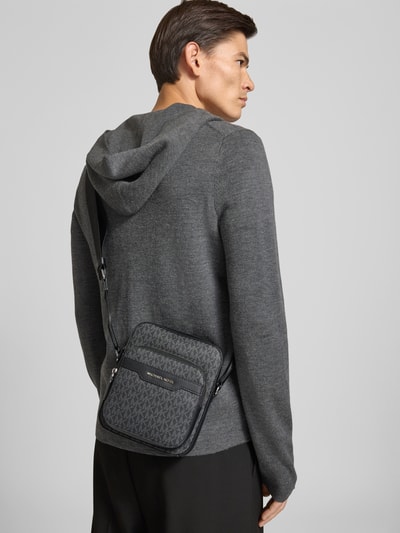 Männermodel trägt Umhängetasche mit Logo-Muster Modell 'HUDSON' von Michael Kors in grau mit all-over look, labeldetail, schouderband, ganzkörperansicht rückansicht. Heren, schoudertas met logomotief, hoofvak met ritssluiting, breedte 19 cm, lengte 25 cm, diepte 9 cm, bandlengte 104 cm.