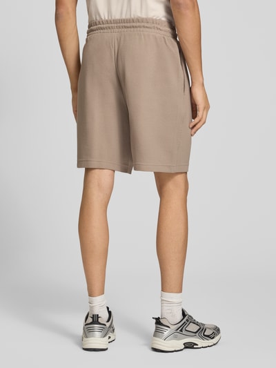 Männermodel trägt Relaxed Fit Sweatshorts aus Baumwoll-Mix 'ESS ELEVATED' von PUMA in Beige, strukturierte Oberfläche, Herren Sweatshorts, Ganzkörperansicht Rückansicht.