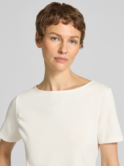 Kobiece modelka nosi T-Shirt in asymmetrischer Form Modell 'Helle' od My Essential Wardrobe, kolor kremowy, mieszanka materiałów z udziałem wiskozy, okrągły dekolt, drapowania, kontekst: damska koszulka, długość tyłu w rozmiarze S: 60 cm, zbliżenie na górną część ciała.