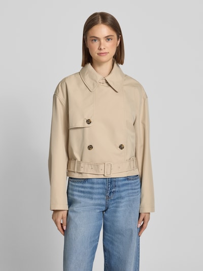 Kobiece modelka nosi Relaxed Fit Trenchcoat aus Baumwoll-Mix od Tommy Jeans, efekt: jednolity kolor, mieszanka bawełny, splot twill, wykładany kołnierz, krój relaxed fit, długi rękaw, zapięcie: listwa guzikowa 2-rzędowa, pasek w talii z klamrą, naszywka z logo, kieszeń wewnętrzna, skrócony krój, widok całej sylwetki z przodu.