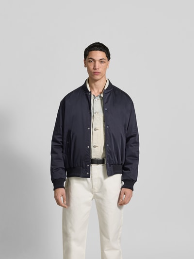 Männermodel trägt Blouson mit Stehkragen von MAISON KITSUNÉ in Dunkelblau, lockere Passform, Druckknopfleiste, Ganzkörperansicht von vorne.