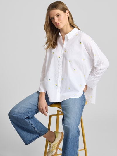 Frauenmodel trägt Relaxed Fit Hemdbluse aus reiner Baumwolle Modell 'NEW LINA GRACE' von Only in Weiß mit Herz-Stickereien, Knopfleiste und Hemdblusenkragen, kombiniert mit blauer Jeans; Nahaufnahme Oberkörper.