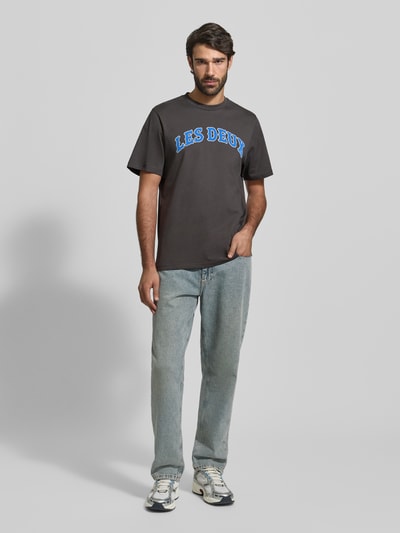 Męski model nosi T-shirt mit Label-Print Modell 'Brady' von Les Deux, bawełna, krój regular fit, okrągły dekolt, długość tyłu 71 cm, Ganzkörperansicht von vorne