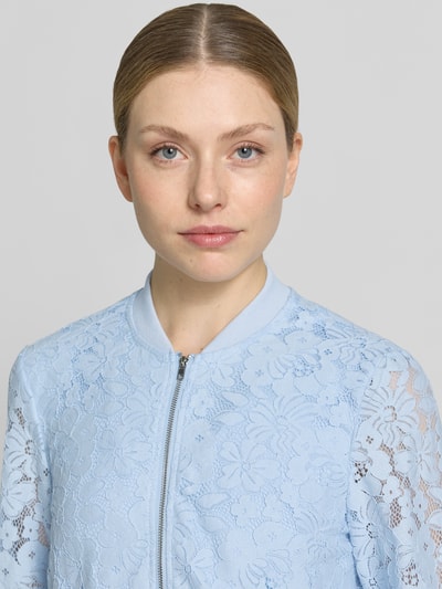 Frauenmodel trägt Regular Fit Blouson aus Baumwoll-Mix Modell 'HONEY' von Vero Moda mit florales Allover-Muster, Häkel-Optik, College-Kragen, Reißverschluss, Langarm, geripptem Ärmelabschluss und Rumpfabschluss, Farbe Hellblau, Materialverarbeitung: Baumwoll-Mix, Nahaufnahme Oberkörper.