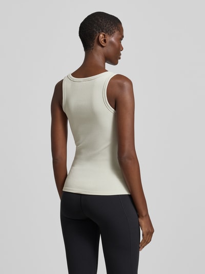 Frauenmodel trägt Slim Fit Top aus Viskose-Mix Modell 'Colette' von Guess Activewear in Hellbeige, glatte Textur, Ganzkörperansicht Rückansicht.