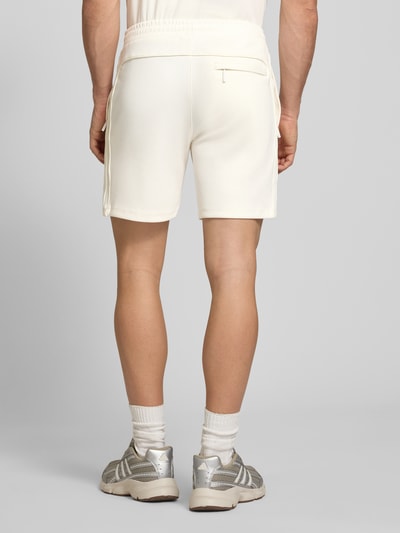 Männermodel trägt Shorts mit Logo-Stitching Modell 'EGEO' von SERGIO TACCHINI, cremeweiß, lockerer Schnitt, Rückansicht Ganzkörperansicht.