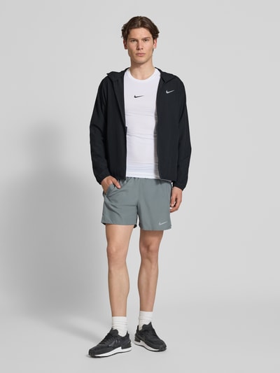 Männermodel trägt Trainingsjacke mit Logo-Print und Stehkragen von NIKE TRAINING in Schwarz, gerader Schnitt, Reißverschluss, seitliche Eingrifftaschen, elastische Ärmelabschlüsse, Rückenlänge 69 cm, Ärmellänge 65 cm, Ganzkörperansicht von vorne.