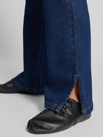 Frauenmodel trägt Straight Fit Jeans mit Gehschlitzen von MYON, dunkelblaue Farbe, glatte Textur, Detailaufnahme Unterschenkel, 5-Pocket-Design, Knopf- und Reißverschluss, Bundweite 40 cm, Innenbeinlänge 82 cm.