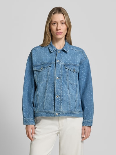 Frauenmodel trägt Regular Fit Jeansjacke mit Logo-Patch Modell 'ARCATA' von Mustang aus Elastischer-Baumwoll-Mix, mittleres Blau, Kontrastnähte, Umlegekragen, Brusttaschen, durchgängige Knopfleiste, Eingrifftaschen, Ganzkörperansicht von vorne.