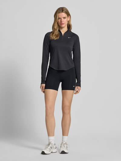 Frauenmodel trägt Radlerhose mit elastischem Bund und Logo von NIKE TRAINING, schwarzer Material-Mix mit Stretch-Anteil, körpernahe Passform, Ganzkörperansicht von vorne.