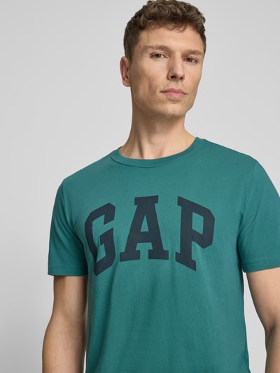 Männermodel trägt T-Shirt mit Logo und Rundhalsausschnitt von GAP in Türkis, Reine Baumwolle, Regular-Fit, Logo, Nahaufnahme Oberkörper. Rückenlänge bei Größe M: 72 cm.