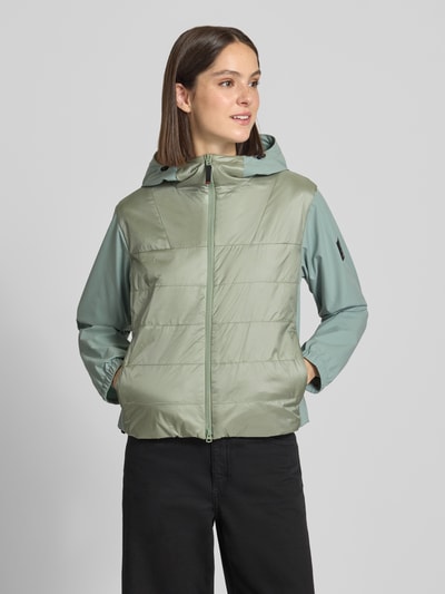 Modelka nosi kurtkę damską o kroju regular fit FIRE + ICE Jacke mit Zweiwege-Reißverschluss Modell 'MARTA' z kapturem z tunelem, jasnozielony kolor, tekstura gładka i pikowana, szerokość ramion w rozmiarze 36: 46 cm, szerokość w rozmiarze 36: 53 cm, długość tyłu w rozmiarze 36: 57 cm, długość rękawów w rozmiarze 36: 62 cm, zamek błyskawiczny dwustronny, widok całej sylwetki z przodu.
