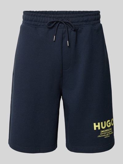 Produktfoto, dunkelblaue Loose Fit Sweatshorts aus reiner Baumwolle Modell 'NOMARIO' von Hugo Blue mit gelbem Logo Print, Tunnelzugbund, seitlichen Eingrifftaschen und aufgesetzter Gesäßtasche, unifarbene Optik, glatte Textur.