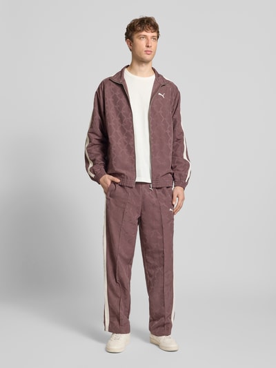 Męski model nosi Straight Fit Sweatpants mit Logo-Stitching od PUMA PERFORMANCE, krój straight fit, elastyczny pas, kieszenie, ozdobne szwy, nadruk logo, kolor brązowy, całkowity widok z przodu.