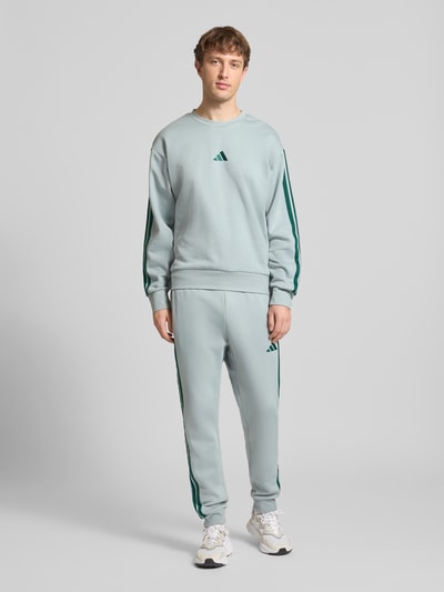 Männermodel trägt Sweatshirt mit Rundhalsausschnitt und Logo von adidas Sportswear, hellgrau, Regular-Fit, Baumwoll-Mix mit Viskose-Anteil, Ganzkörperansicht von vorne.