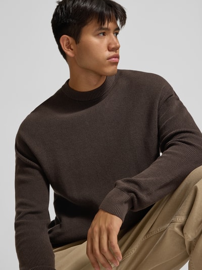 Männermodel trägt Regular Fit Strickpullover aus reiner Baumwolle von REVIEW in Dunkelbraun mit Rundhalsausschnitt, Nahaufnahme Oberkörper.