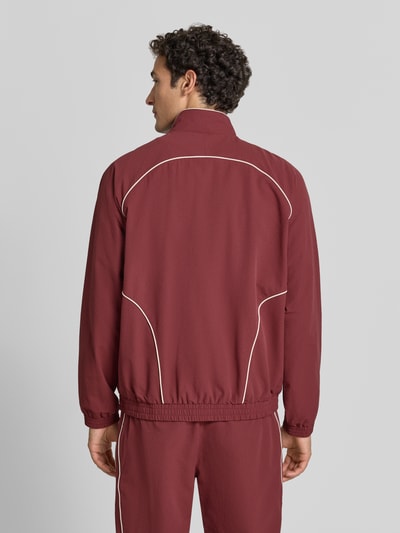 Männermodel trägt Trainingsjacke mit Label-Stitching Modell 'Seersucker' von Les Deux in Rot mit weißen Kontrastpaspeln, Ganzkörperansicht Rückansicht. Gerader Schnitt, Stehkragen, Zwei-Wege-Reißverschluss, elastische Abschlüsse und strukturierte Seersucker-Textur, Rückenlänge bei Größe M: 68 cm, Ärmellänge bei Größe M: 83 cm.