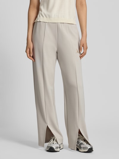Vrouwenmodel draagt Straight Fit Sweatpants uit elastische viscosemix van Armani Exchange, beige kleur, labeldetail, pijpsplitten, elastische band, binnenbeenlengte maat S 77 cm, detailopname voorkant.