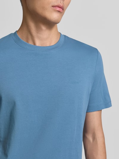 Mężczyzna nosi Regular Fit T-Shirt aus reiner Baumwolle von s.Oliver RED LABEL, unifarben, krótkie rękawy, materiał jersey, detal z napisem, zbliżenie na górną część ciała.