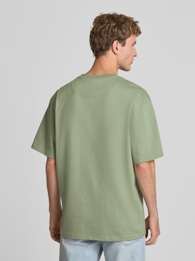 Männermodel trägt T-Shirt mit Logo und Rundhalsausschnitt von Karl Kani aus reiner Baumwolle, relaxed Fit, Rückenlänge 77 cm, Ganzkörperansicht Rückansicht