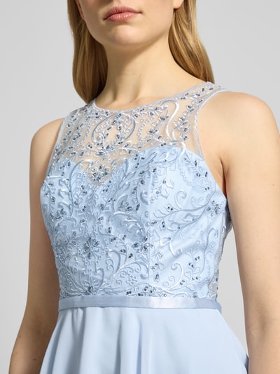 Vrouwenmodel draagt Cocktailjurk met strass-steentjes van Luxuar, effen design, semi-transparant, ronde hals, licht getailleerd model, knielengte, ritssluiting, detailopname bovenlichaam.