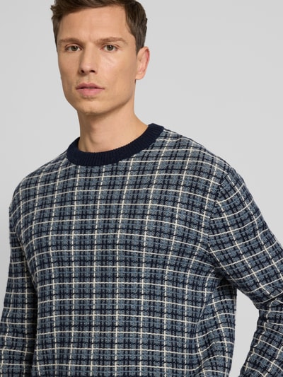 Männermodel trägt Regular Fit Strickpullover aus Woll-Mix Modell 'MIKOLAS' von SELECTED HOMME mit blauw geruit patroon, crew neck, geribde boorden, gebreide textuur, Nahaufnahme Oberkörper.