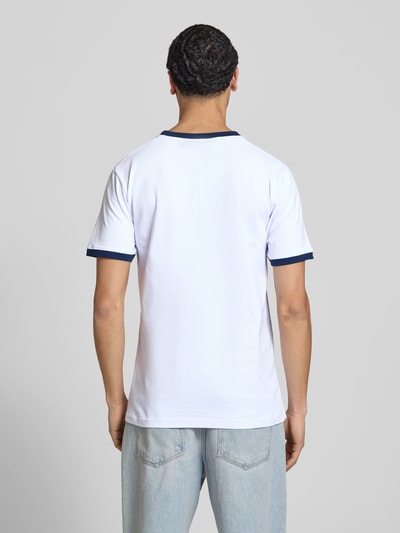 Męski model nosi T-shirt z logo i łatką label 'RINGETTO' od Ellesse z czystej bawełny, prosty krój, biały kolor, widok całej sylwetki od tyłu