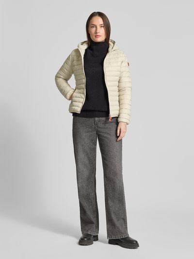 Frauenmodel trägt Steppjacke mit Kapuze Modell 'DAISY' von SAVE THE DUCK in Hellbeige, körpernah geschnitten, glatte Textur, Ganzkörperansicht von vorne.
