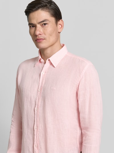 Männermodel trägt Regular Fit Freizeithemd aus reinem Leinen Modell 'RELEGANT' von BOSS Orange in zartem Rosa, Optik: Unifarben, Flammgarn-Textur, Kentkragen, durchgehende Knopfleiste, Label-Stitching, Langarm, 2-Knopf-Manschetten, Ganzkörperansicht von vorne.
