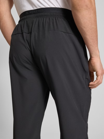 Männermodel trägt Trainingshose mit elastischem Bund und Logo von The North Face aus schwarzem Material-Mix mit Stretch-Anteil, Nahaufnahme Rückansicht.