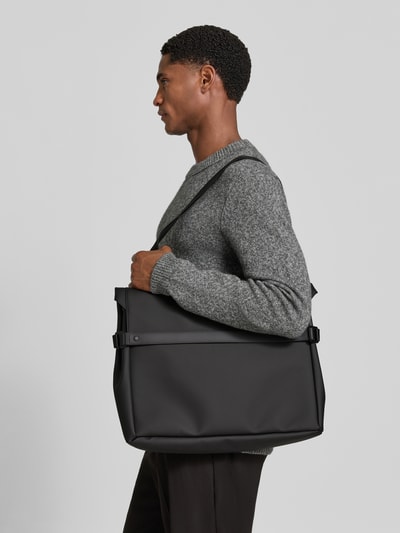 Mannelijk model draagt Messenger Bag met logo-detail van Rains, zwarte tas met overslag, verstelbare schouderband, drukknopen, hoofdkamer, breedte 48 cm, lengte 33 cm, diepte 9 cm, schouderband 82 cm, zijaanzicht, detailopname.