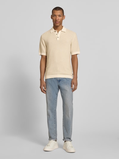 Męski model nosi Regular Fit Poloshirt in Strick-Optik Modell 'Kingsley' von Jack & Jones Premium, bawełna, krój regular fit, imitacja dzianiny, z krótkim rękawem, kołnierzyk polo, elastyczne wykończenia, długość tyłu w rozmiarze M: 77 cm, jasny beżowy, faktura dzianiny, proste kształty, widok całej sylwetki z przodu.