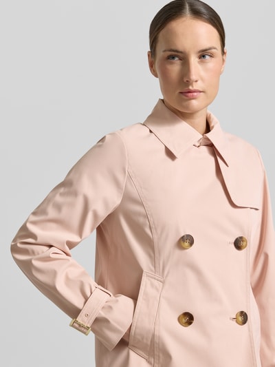 Modelka nosi Trenchcoat mit Knopfverschluss von MICHAEL Michael Kors w kolorze jasnoróżowym, krój regular fit, klasyczny kołnierz, dwurzędowy, tekstura gładka, zapięcie na guziki, zdjęcie: zbliżenie na górną część ciała z przodu, długość tyłu w rozmiarze S: 61 cm, szerokość ramion w rozmiarze S: 40 cm, szerokość w rozmiarze S: 52 cm, długość rękawa w rozmiarze S: 63 cm