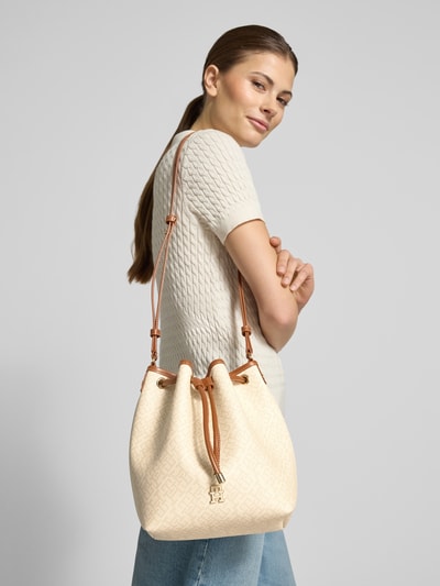 Frauenmodel trägt Umhängetasche mit Logo-Detail Modell 'MONOPLAY BUCKET' von Tommy Hilfiger in beige unifarbener Lederoptik, Allover-Muster, Kunstleder, Schulterriemen, Ganzkörperansicht Rückansicht.