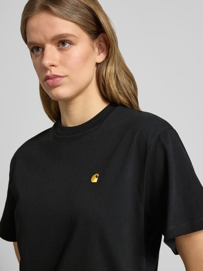Frauenmodel trägt T-Shirt mit Label-Stitching von Carhartt Work In Progress aus reiner Bio-Baumwolle, Relaxed-Fit, Rundhalsausschnitt, Nahaufnahme Oberkörper.