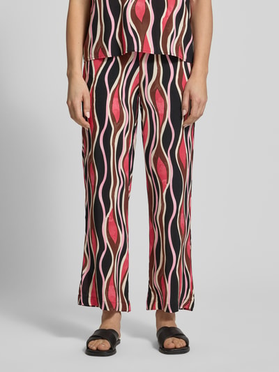 Frauenmodel trägt Straight Fit Stoffhose aus reiner Viskose Modell 'Cammi' von Soyaconcept, grafisches Muster in Rot, Beige und Schwarz, elastischer Bund mit Tunnelzug, Bundweite bei Größe S 35 cm, Innenbeinlänge 74 cm, Ganzkörperansicht von vorne.